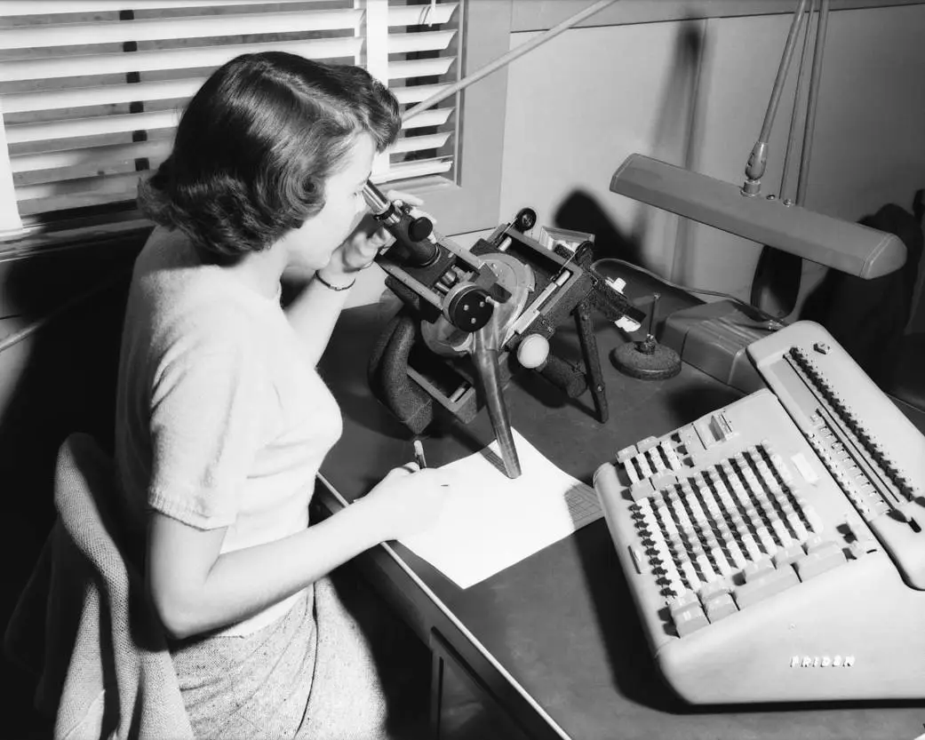 a black and white photo of a woman sitting at a desk with instruments, further described below